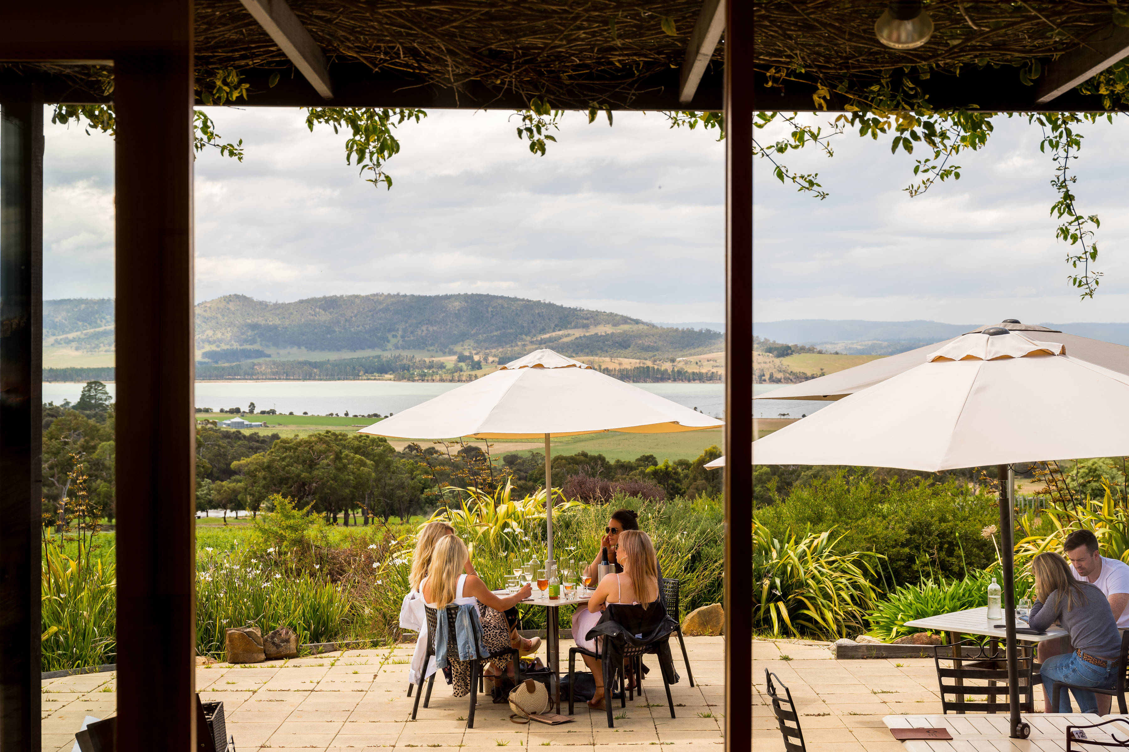 Guests seated at tables under umbrellas enjoying wine tasting on the Coal Valley Vineyard patio, overlooking Barilla Bay in the distance.