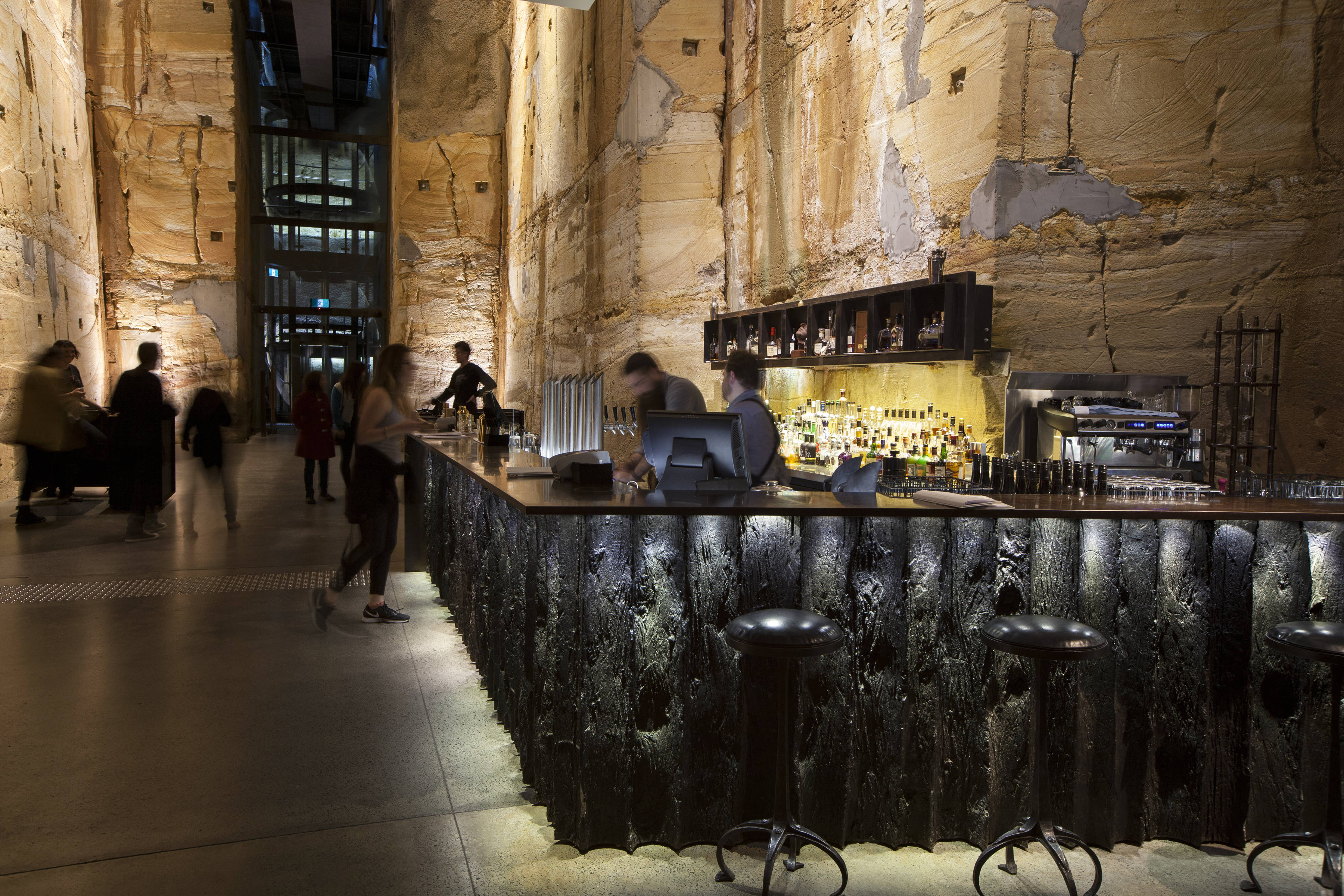 Void Bar at Mona featuring cocktail bar in front of a towering sandstone wall.